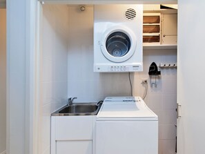Ein kleiner Hauswirtschaftsraum mit einer Waschmaschine und einem Trockner mit Frontlader, einem Waschbecken und einem an der Wand montierten Heizgerät.