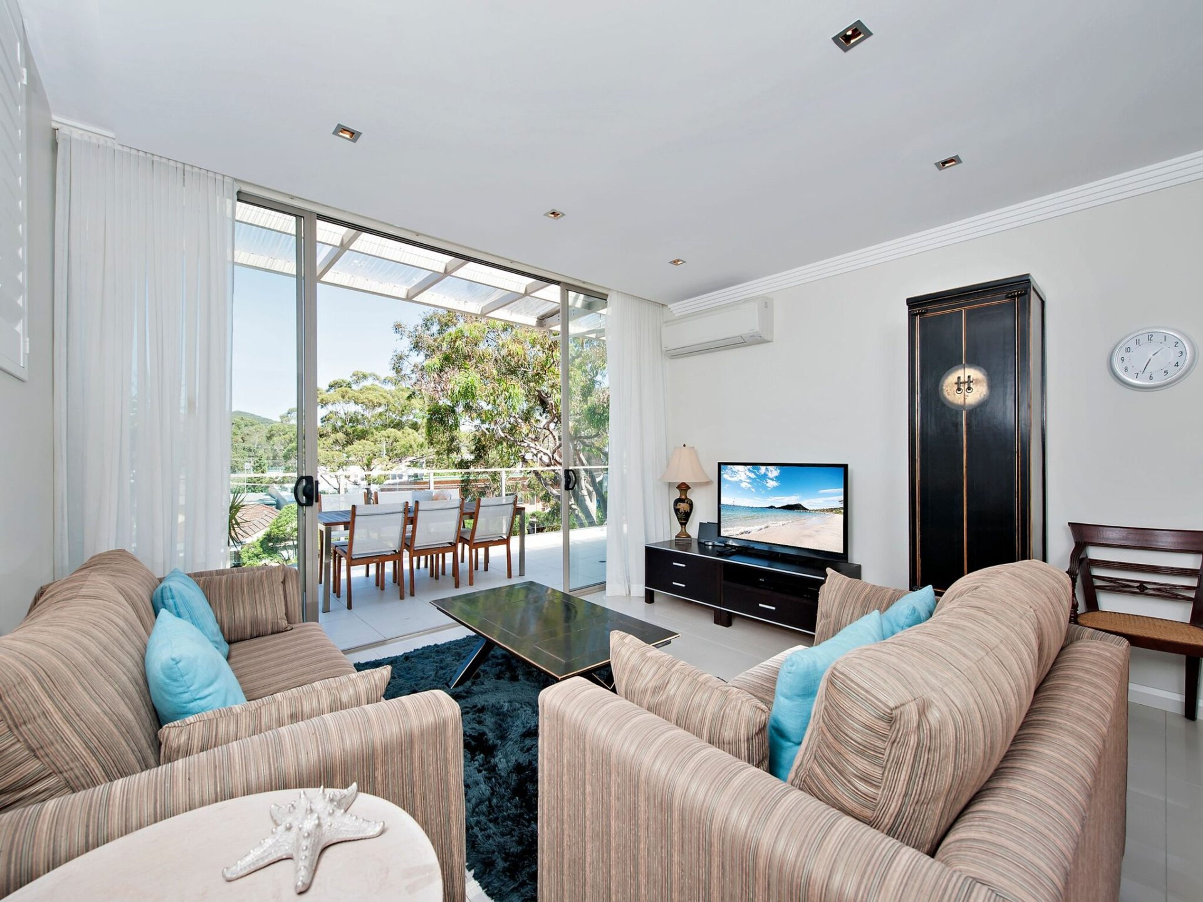 A living room with a sofa set, a coffee table, a television, and a view of the outdoors.