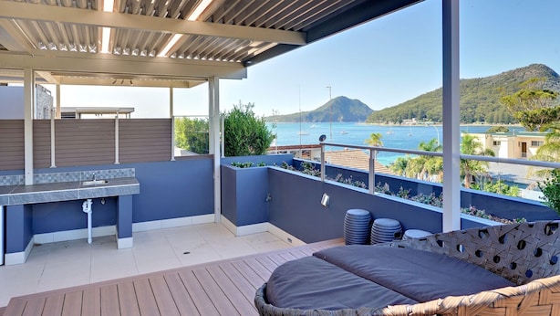 A balcony with a seating area, a built-in grill, and a view of the sea and hills. - Aura Apartments U12 Shoal Bay Beach Views (Shoal Bay)