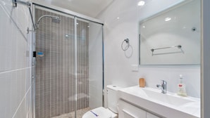 A modern bathroom with a glass-enclosed shower, a toilet, and a vanity with a mirror and toiletries. - Aura Apartments U12 Shoal Bay Beach Views (Shoal Bay)