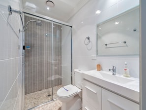 Een moderne badkamer met een douchecabine van glas, een toilet en een wastafel met spiegel en toiletartikelen.