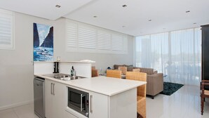 A modern kitchen with a built-in oven and microwave, a dining area with wicker furniture, and a large window offering a view of the city.
