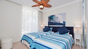 A bedroom with a large bed, two bedside tables, a ceiling fan, and a painting of a wave.