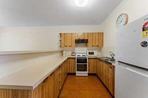 A compact kitchen with wooden cabinets, a microwave, a stove, and a refrigerator. - Shoal Bay Av 1 Ground floor (Shoal Bay)