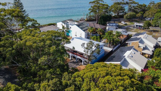 A residential area with houses, some with solar panels, surrounded by dense greenery and a view of the sea. - Beach break garden unit! (Shoal Bay)