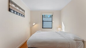 A bedroom with a bed, a window, a wall-mounted artwork, and a floor lamp. - Beach break garden unit! (Shoal Bay)