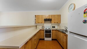 A compact kitchen with wooden cabinets, a microwave, an oven, and a refrigerator. - Beach break garden unit! (Shoal Bay)