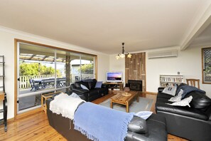 Ein Wohnzimmer mit einem großen Schiebeglastür, die auf eine Terrasse im Freien führt, einem Kamin und einem Fernseher.