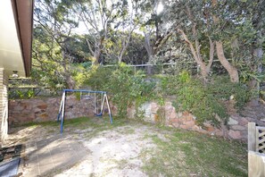 A backyard with a swing set, stone wall, and trees.