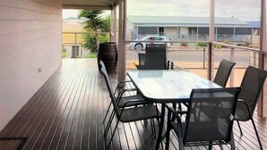 A covered outdoor area with a table and chairs, a wooden deck, and a view of a building and a car in the background. - Livin' The Dream ~ Spacious  ~  Off Peak Special! WIFI Available (Point Turton)