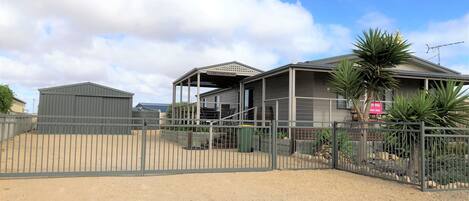 A property with a fenced driveway, a covered outdoor area, and a building with a sign indicating a sale.