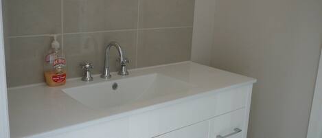 A bathroom with a white sink, two faucets, and a bottle of soap.
