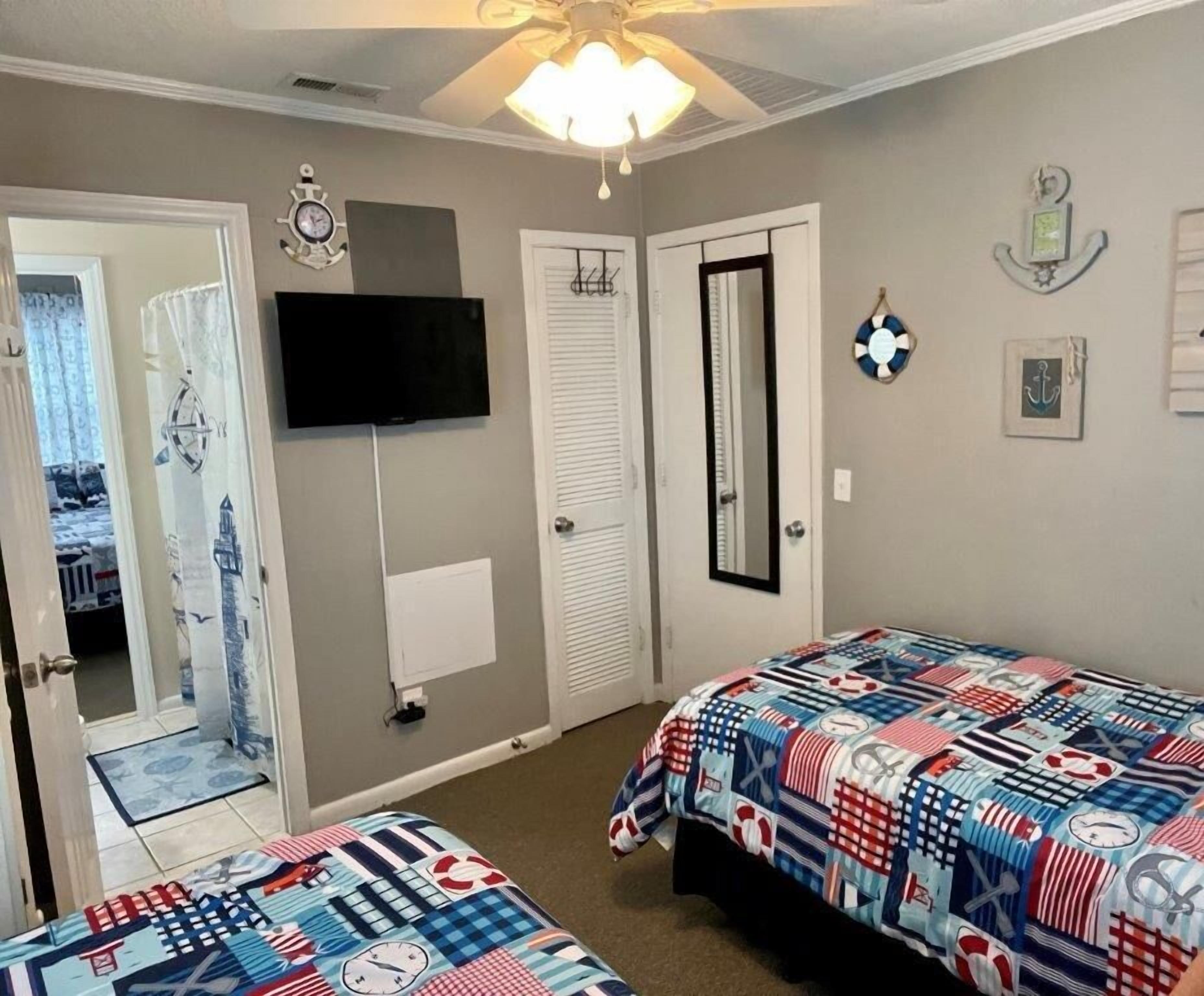 Une chambre avec deux lits, un ventilateur de plafond, une télévision et une décoration sur le thème de la marine.