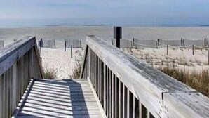 A wooden boardwalk leading to a beach with a fence in the background. - Experience beachfront living at Sandy Bottoms in Holden Beach, NC—perfect for families! (Holden Beach)