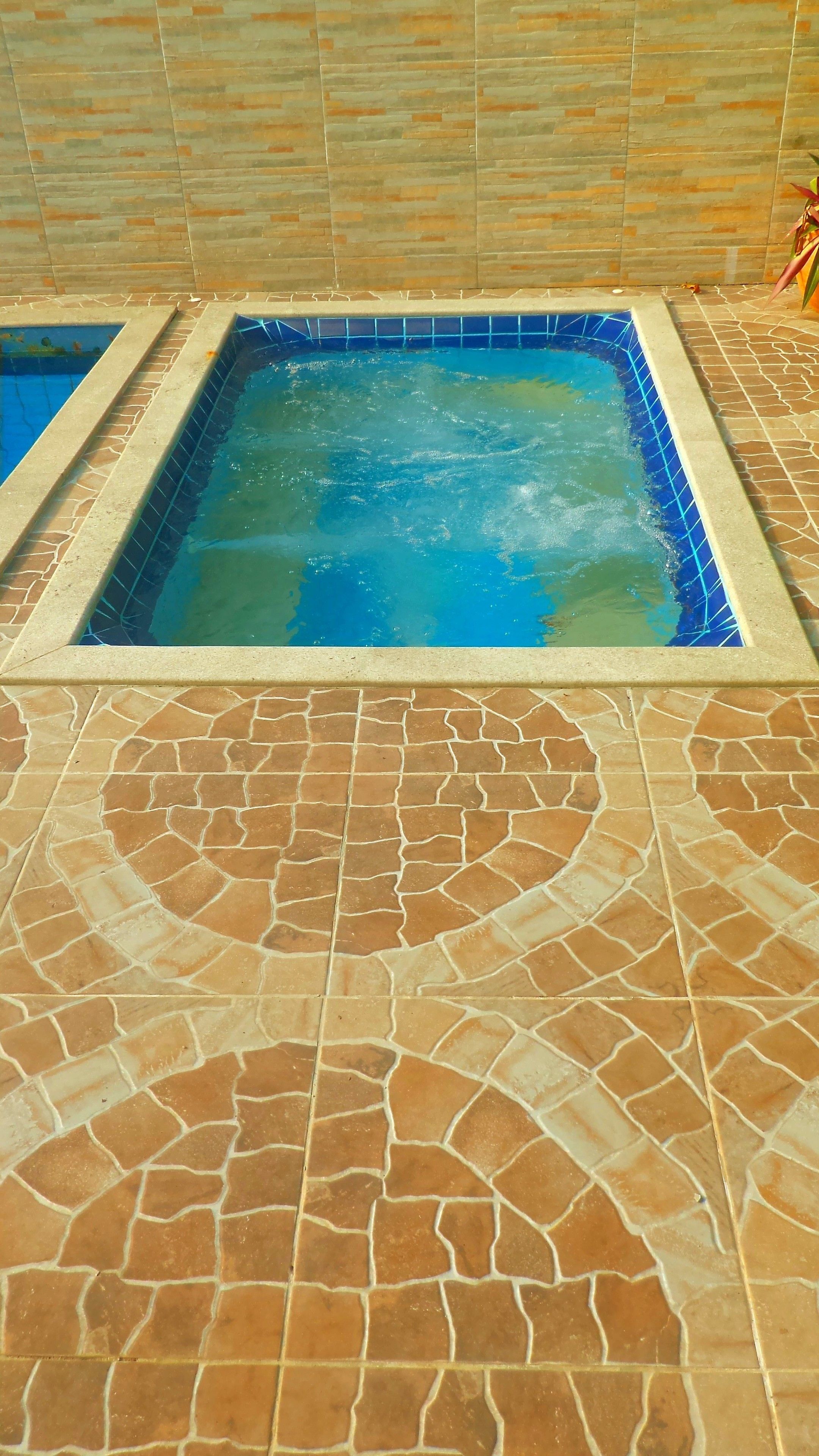 A swimming pool with a blue tiled interior and a patterned tile floor.
