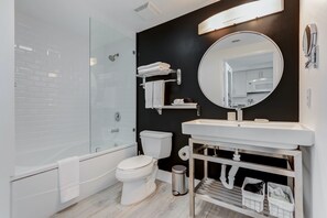 Un baño moderno con cabina de ducha de vidrio, inodoro blanco, bañera, tocador con espejo y una pared de acento negra.