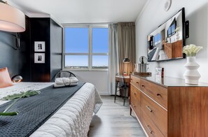 Un dormitorio moderno con una cama grande, un escritorio y vistas de la ciudad a través del ventanal.