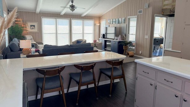 A modern kitchen with a central island, bar stools, and a dining table. - Enjoy oceanfront views at How Sweet The Sound in Holden Beach, NC; perfect for families. (Holden Beach)