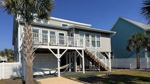 A two-story house with a balcony, a garage, and a sandy driveway. - Enjoy oceanfront views at How Sweet The Sound in Holden Beach, NC; perfect for families. (Holden Beach)