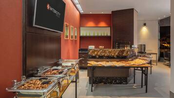 A buffet setup with various food items, a television screen displaying the hotel name, and a modern interior design.