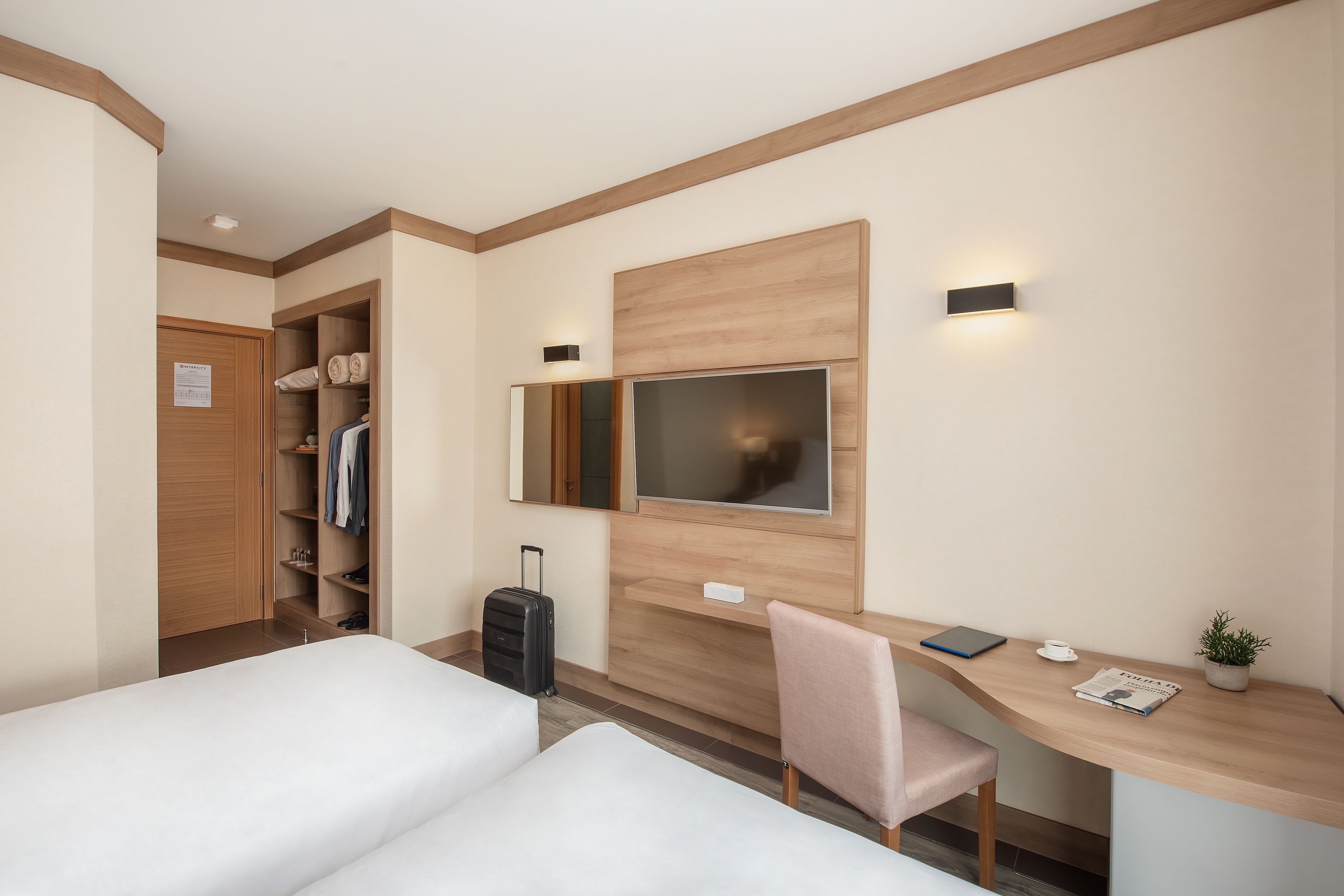 Habitación de hotel con dos camas, un escritorio, un televisor, un armario y una maleta.