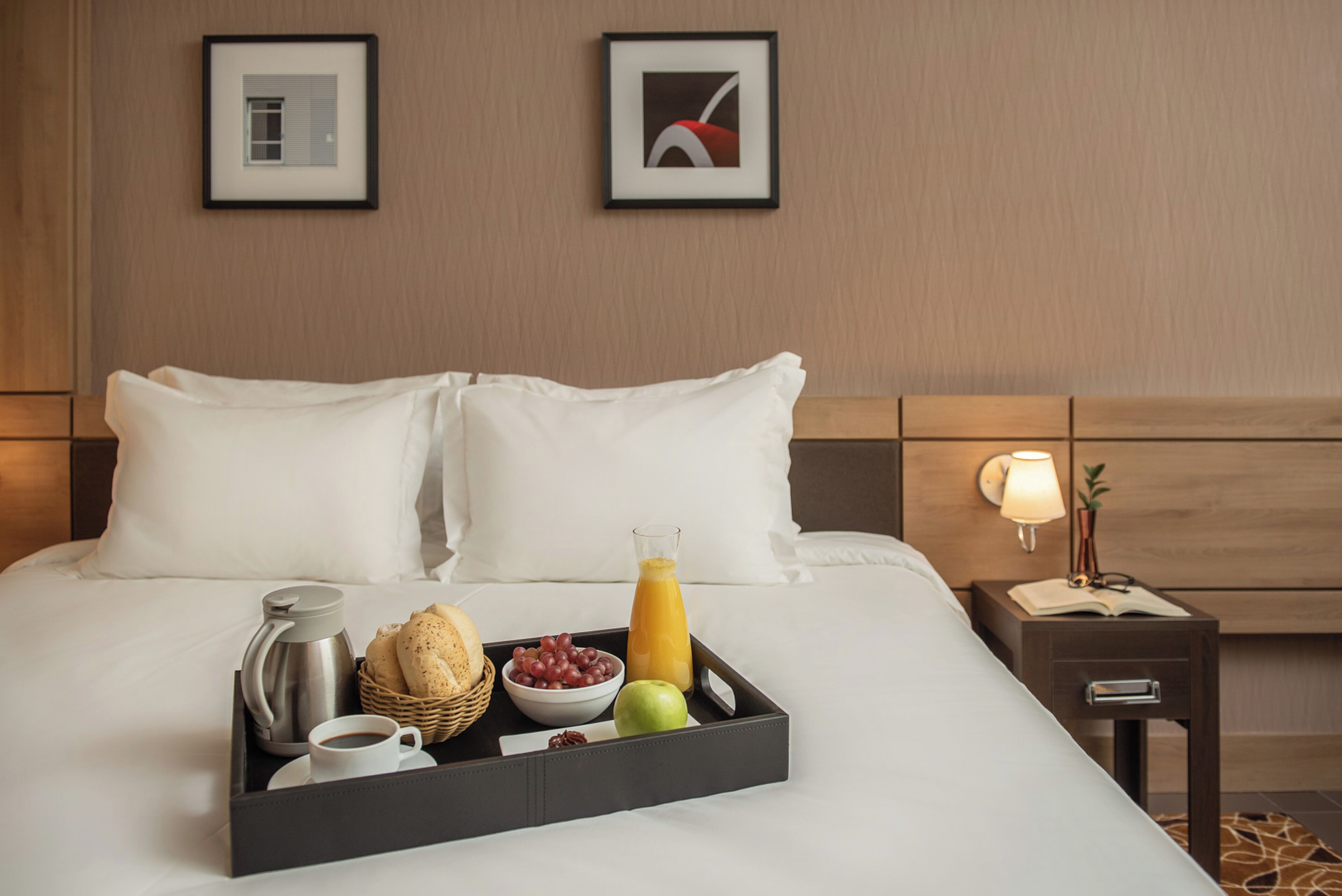 Cama bem arrumada com uma bandeja de itens de café da manhã, incluindo café, pão, uvas e um copo de suco de laranja.