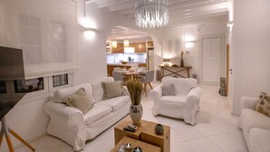 A modern living room with white furniture, a coffee table, and a chandelier. - Mykonian house in Elia beach by GHH (Mykonos)