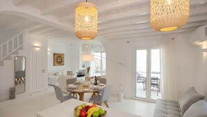 A spacious living area with a dining table set, a sofa, and a fruit bowl on a counter. - Mykonian house in Elia beach by GHH (Mykonos)