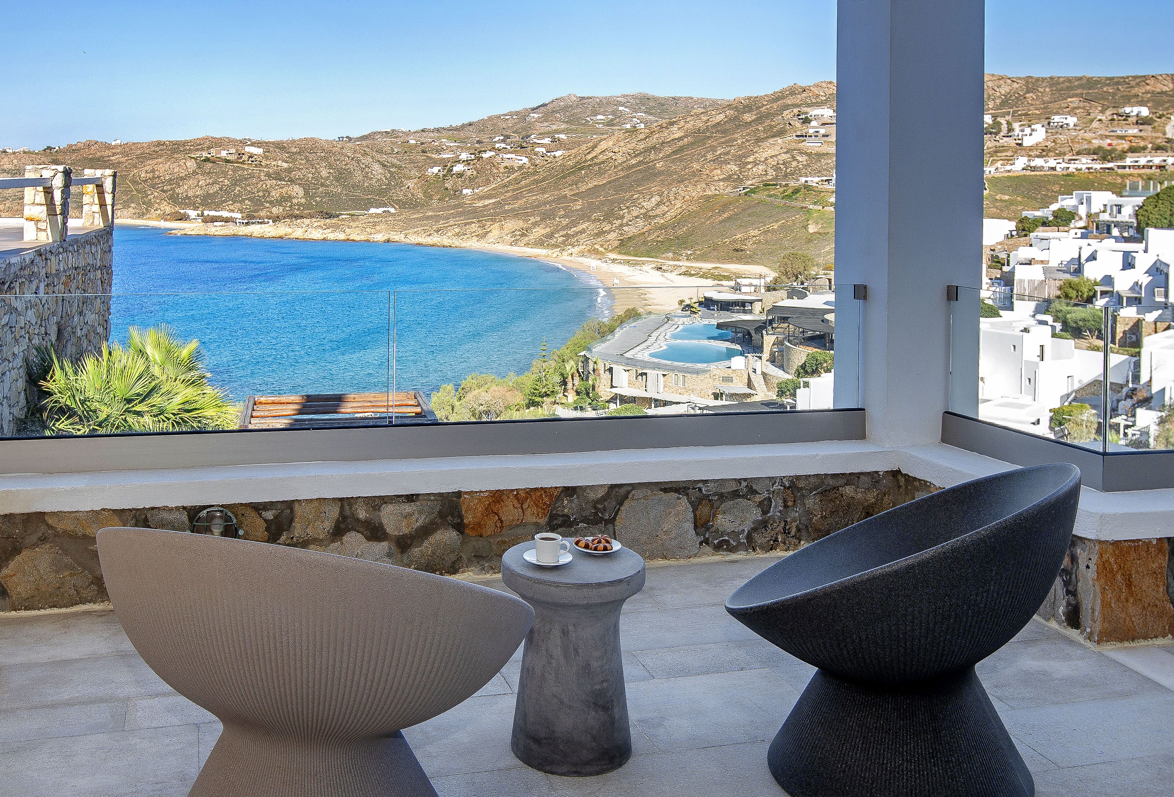 Un balcón con vista al mar, paredes de piedra y una pequeña mesa con una taza y platillo.