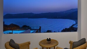 A room with a large window overlooking a body of water at dusk, two wicker chairs, and a small table with a candle. - Mykonian house in Elia beach by GHH (Mykonos)