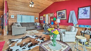 A cozy cabin interior with wooden ceilings, a red accent wall, and a variety of seating options including a sofa and chairs.