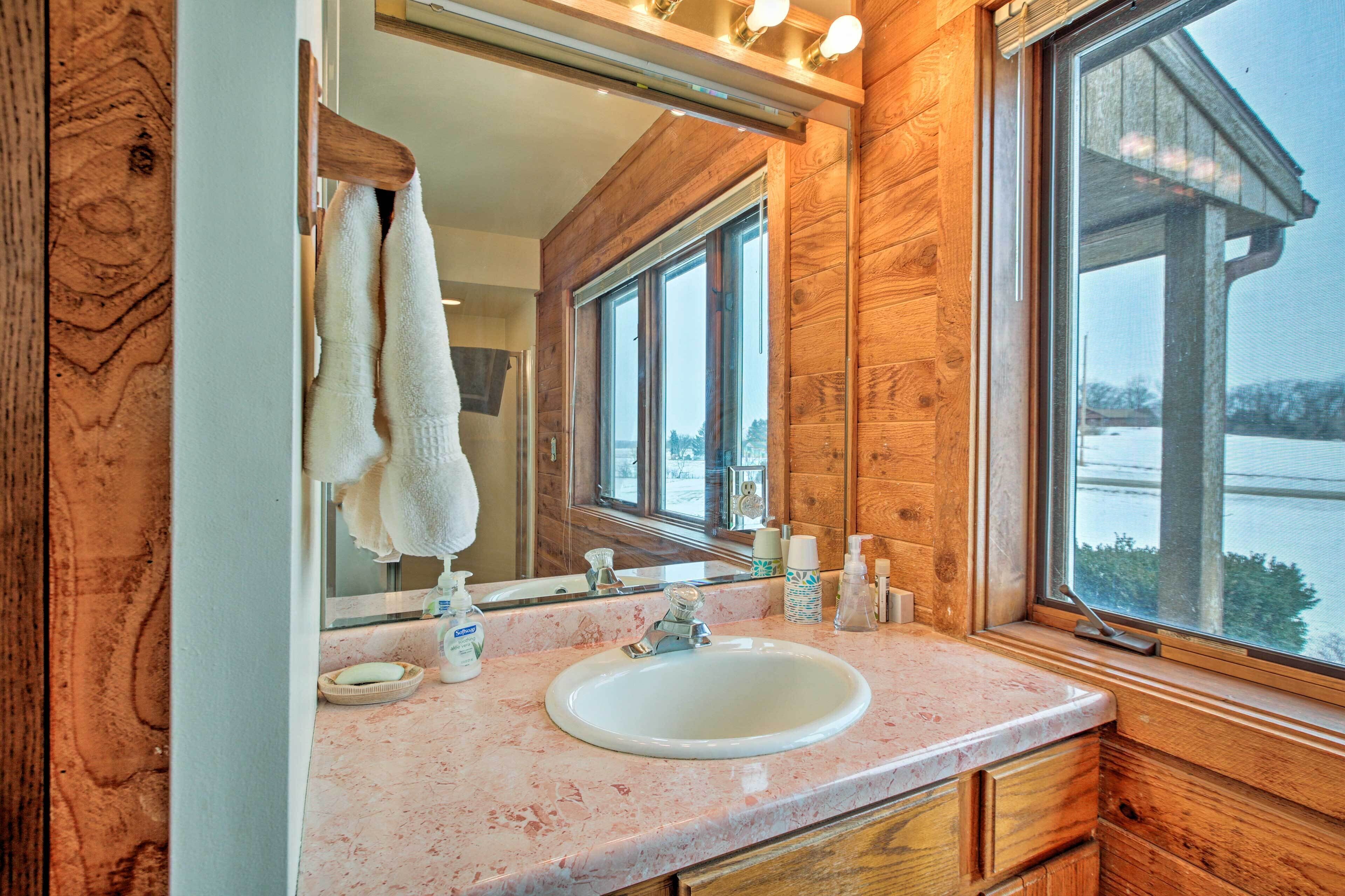 A bathroom with a wooden interior, a large mirror, a sink, and a window with a view of a body of water.