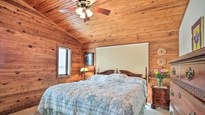 A wooden-paneled bedroom with a bed, dresser, and ceiling fan.