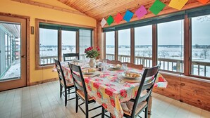 A dining room with a wooden ceiling, large windows, and a table set for four.