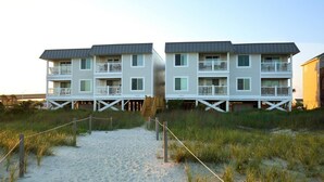 En byggnad som ligger vid stranden, med flera balkonger och en sandstig som leder fram till den.
