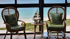 Due sedie in vimini con cuscini verdi e un tavolino con una barchetta a vela in miniatura e un cartello con scritto "BEACH".