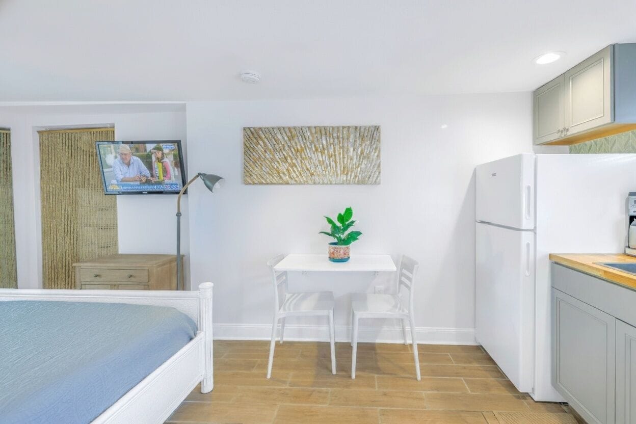 A compact room with a bed, a small table with chairs, a TV, and a refrigerator.