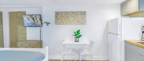 A compact room with a bed, a small table with chairs, a TV, and a refrigerator.