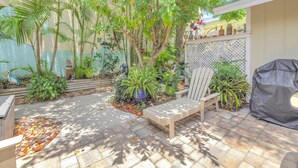 Une terrasse avec un banc en bois, des plantes en pot et un barbecue.