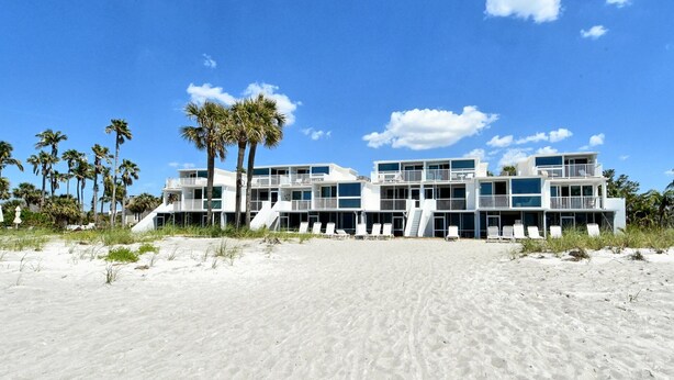 Een strandhotel met meerdere balkons, een zandstrand ervoor en palmbomen.
