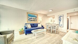 A living room with a blue sofa, a white coffee table, and a dining area with a white table and chairs.