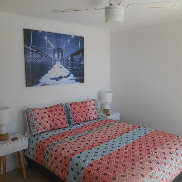 A bedroom with a bed, a nightstand, a lamp, and a ceiling fan.