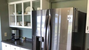 A kitchen with a stainless steel refrigerator, white cabinets, and a coffee maker on the counter. - Tailslide Inn: Spacious 4-bedroom at Holden Beach, perfect for family getaways! (Holden Beach)