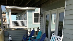 A wooden deck with outdoor seating, a covered area, and a building with a balcony. - Tailslide Inn: Spacious 4-bedroom at Holden Beach, perfect for family getaways! (Holden Beach)