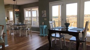 A dining area with a table, chairs, a chandelier, and a view through large windows. - Tailslide Inn: Spacious 4-bedroom at Holden Beach, perfect for family getaways! (Holden Beach)