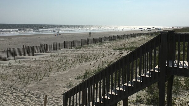 A beach with a wooden fence, a staircase, and the ocean in the background. - Tailslide Inn: Spacious 4-bedroom at Holden Beach, perfect for family getaways! (Holden Beach)
