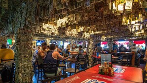 A bar with a ceiling covered in dollar bills, patrons seated at tables, and a neon sign. - Gertrude's Siesta | Top Location! 1-min to Best Beaches, Private Patios, Gate to Village! (Siesta Key)