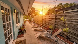 A covered outdoor seating area with lounge chairs and a wooden fence. - Gertrude's Siesta | Top Location! 1-min to Best Beaches, Private Patios, Gate to Village! (Siesta Key)