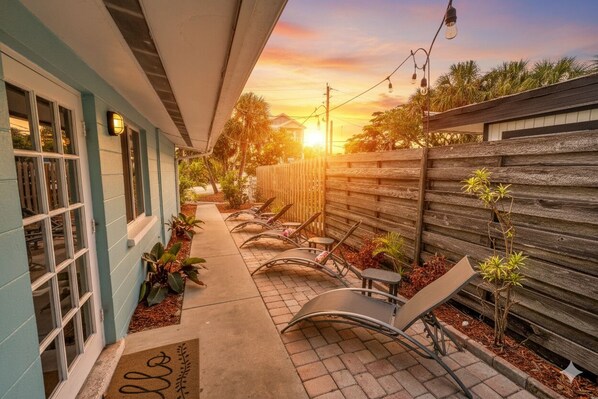 A covered outdoor seating area with lounge chairs and a wooden fence.