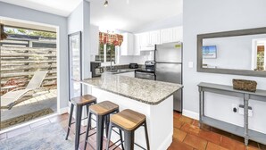 A modern kitchen with a granite countertop, stainless steel appliances, and a large island with bar stools. - Gertrude's Siesta | Top Location! 1-min to Best Beaches, Private Patios, Gate to Village! (Siesta Key)